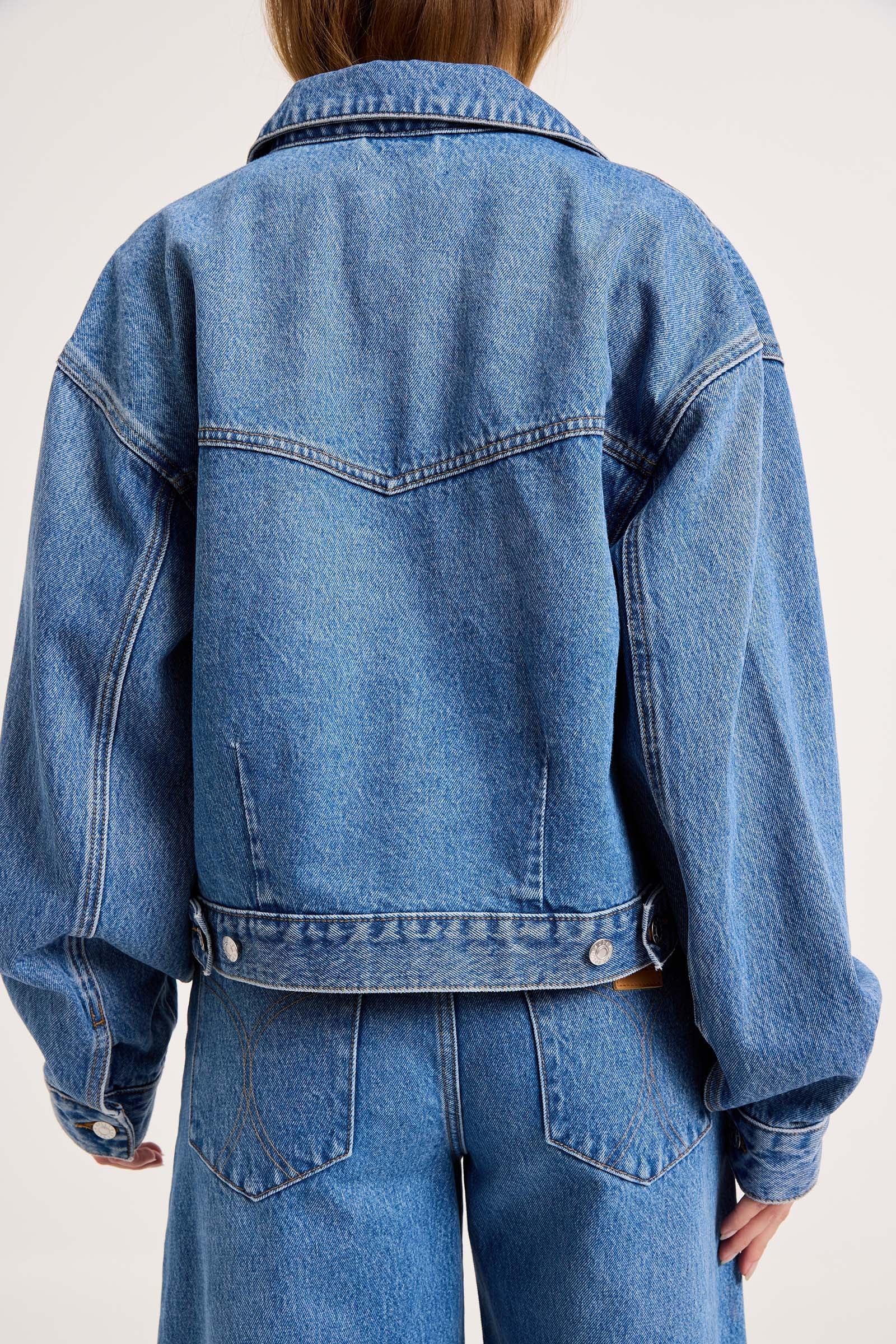 A person shown from the back wearing an oversized light blue denim jacket with matching blue jeans against a plain light background.