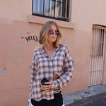 Woman in plaid shirt and shorts standing against a beige wall.
