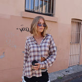 Woman in plaid shirt and shorts standing against a beige wall.