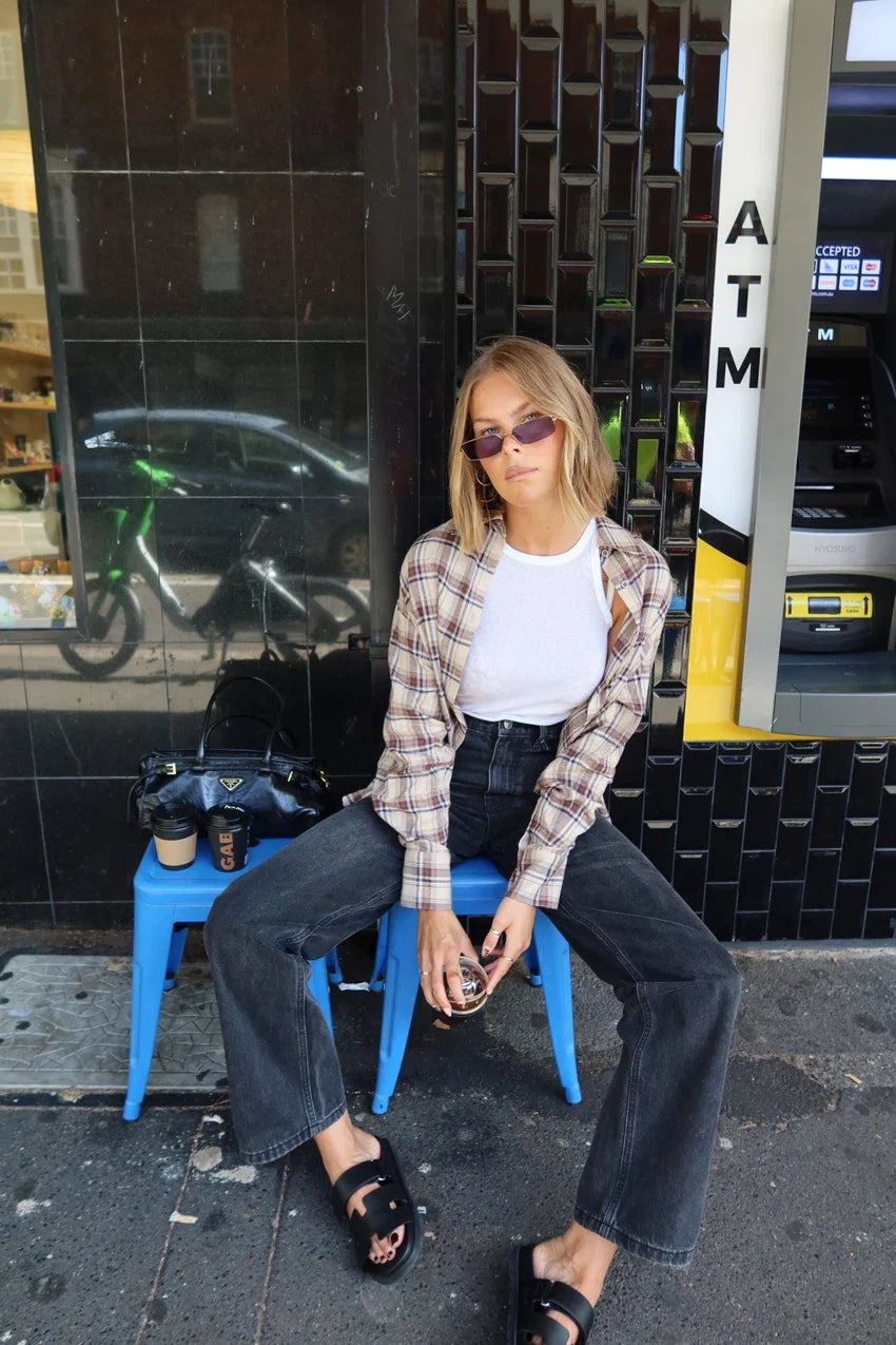 Person sitting on a blue stool wearing sunglasses and a plaid shirt in an urban setting.