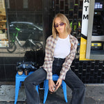 Person sitting on a blue stool wearing sunglasses and a plaid shirt in an urban setting.