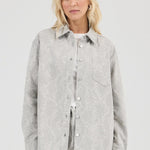 Woman wearing a light gray patterned shirt against a white background