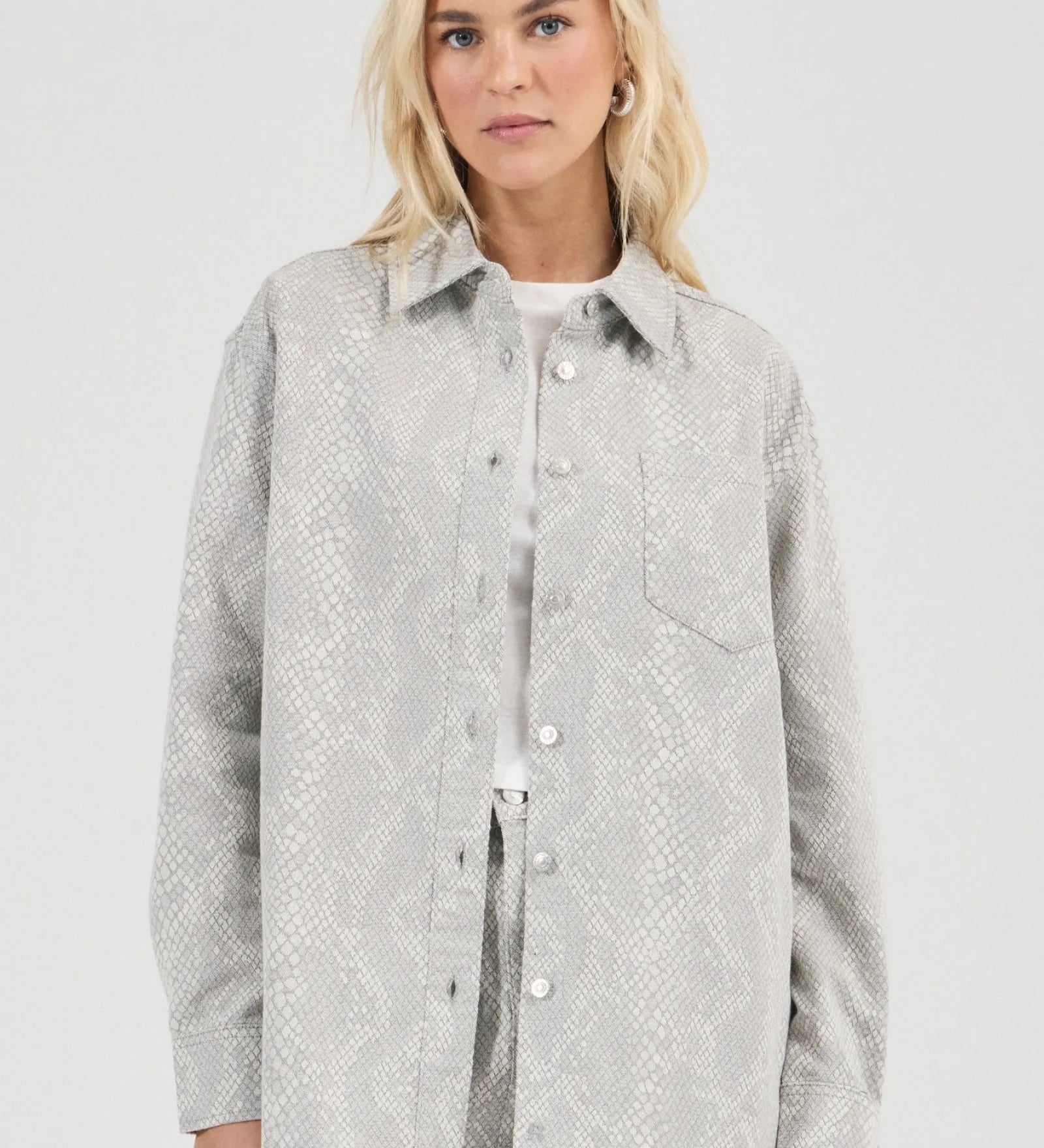 Woman wearing a light gray patterned shirt against a white background