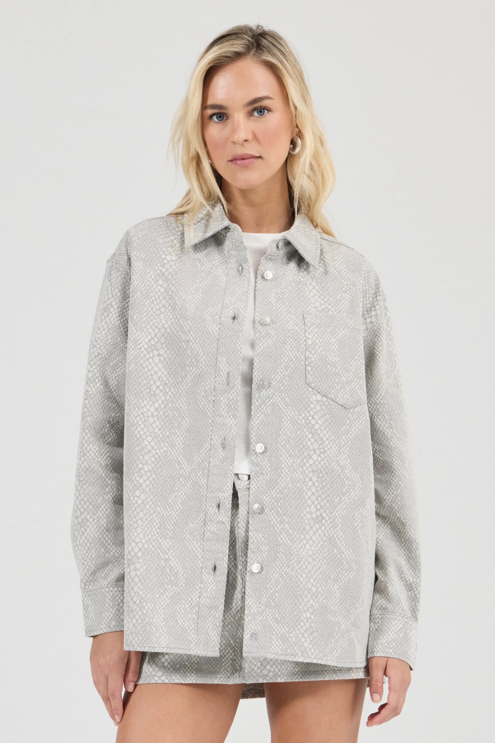 Woman wearing a light gray patterned shirt against a white background