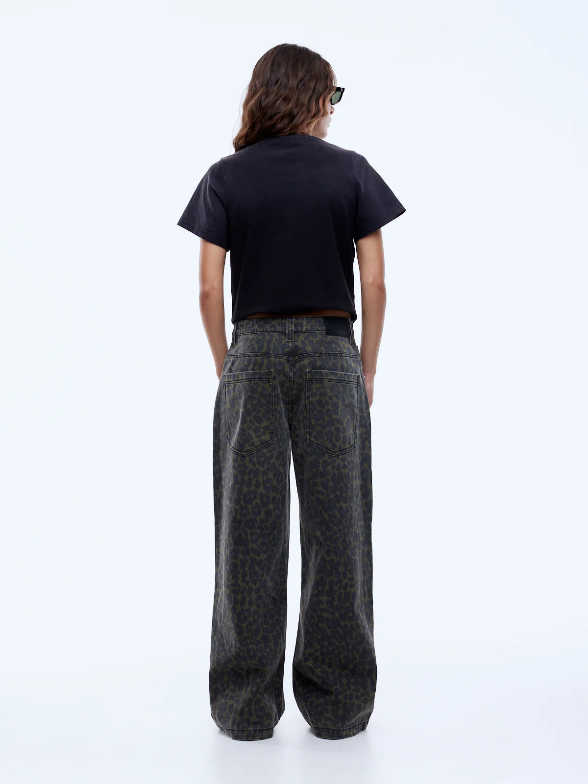 Person wearing a black t-shirt and dark patterned pants on a white background