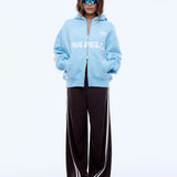 Person wearing a light blue hoodie with a brand logo and black pants on a white background