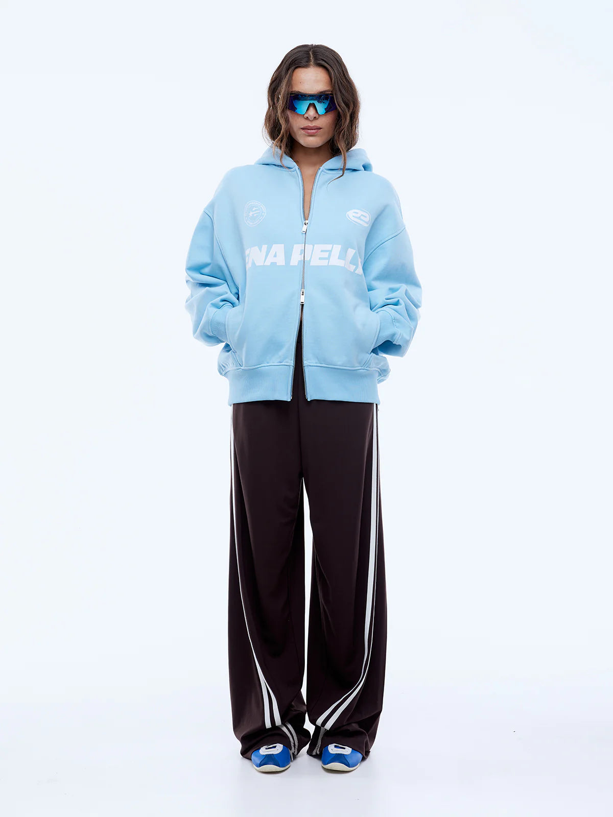 Person wearing a light blue hoodie with a brand logo and black pants on a white background