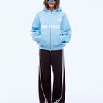 Person wearing a light blue hoodie with branding and dark pants on a white background