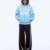 Person wearing a light blue hoodie with branding and dark pants on a white background