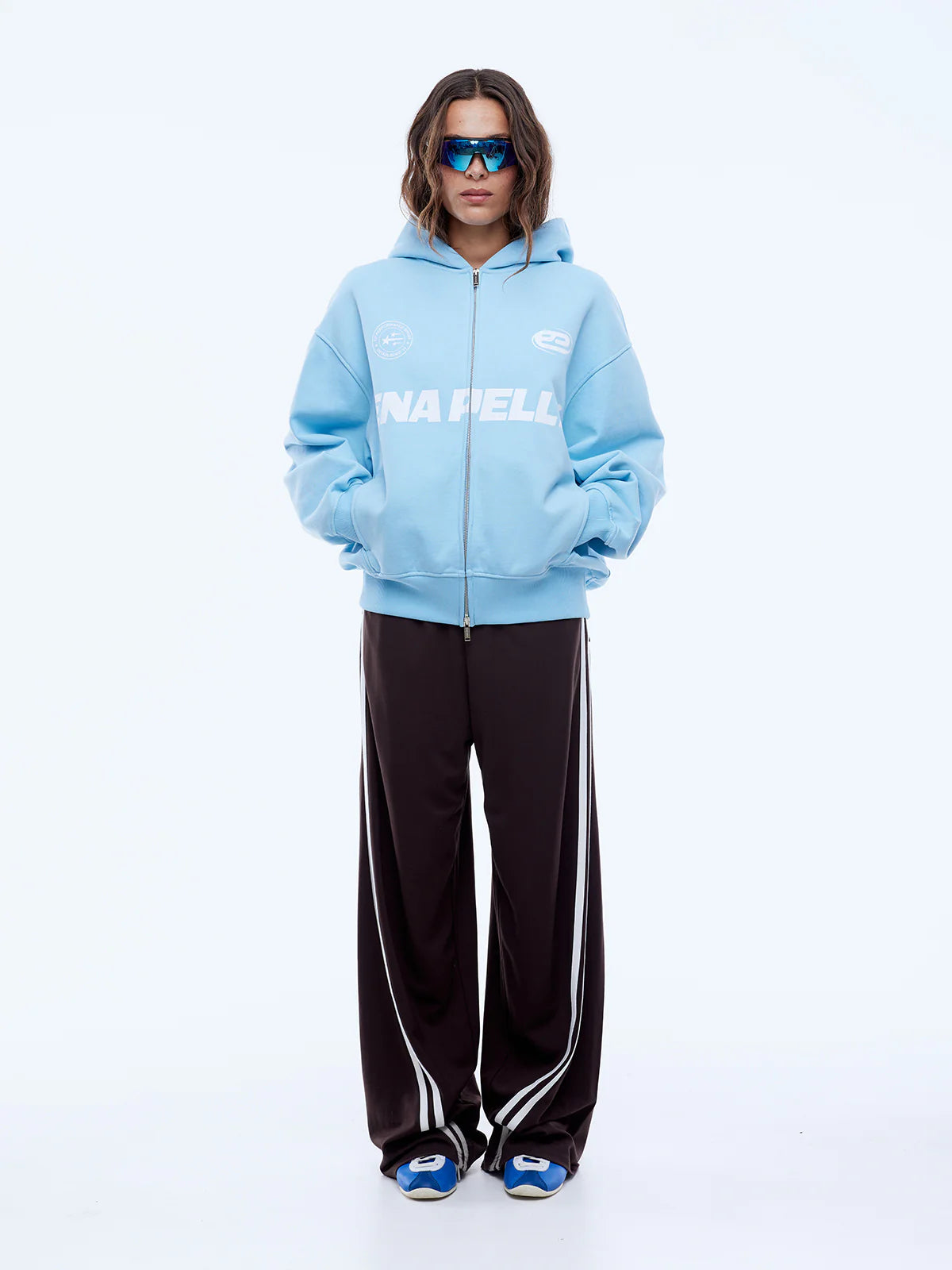 Person wearing a light blue hoodie with branding and dark pants on a white background