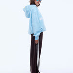 Person wearing a light blue hoodie and dark pants with white stripes on a white background