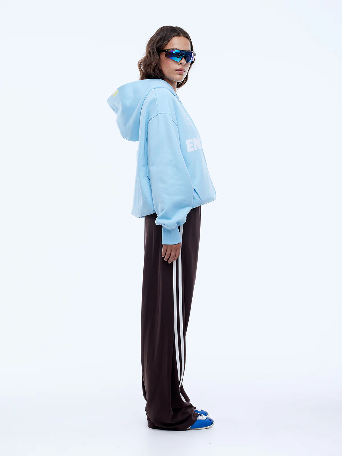Person wearing a light blue hoodie and dark pants with white stripes on a white background
