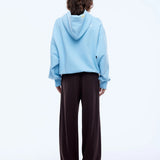 Person wearing a light blue hoodie and dark brown pants on a white background