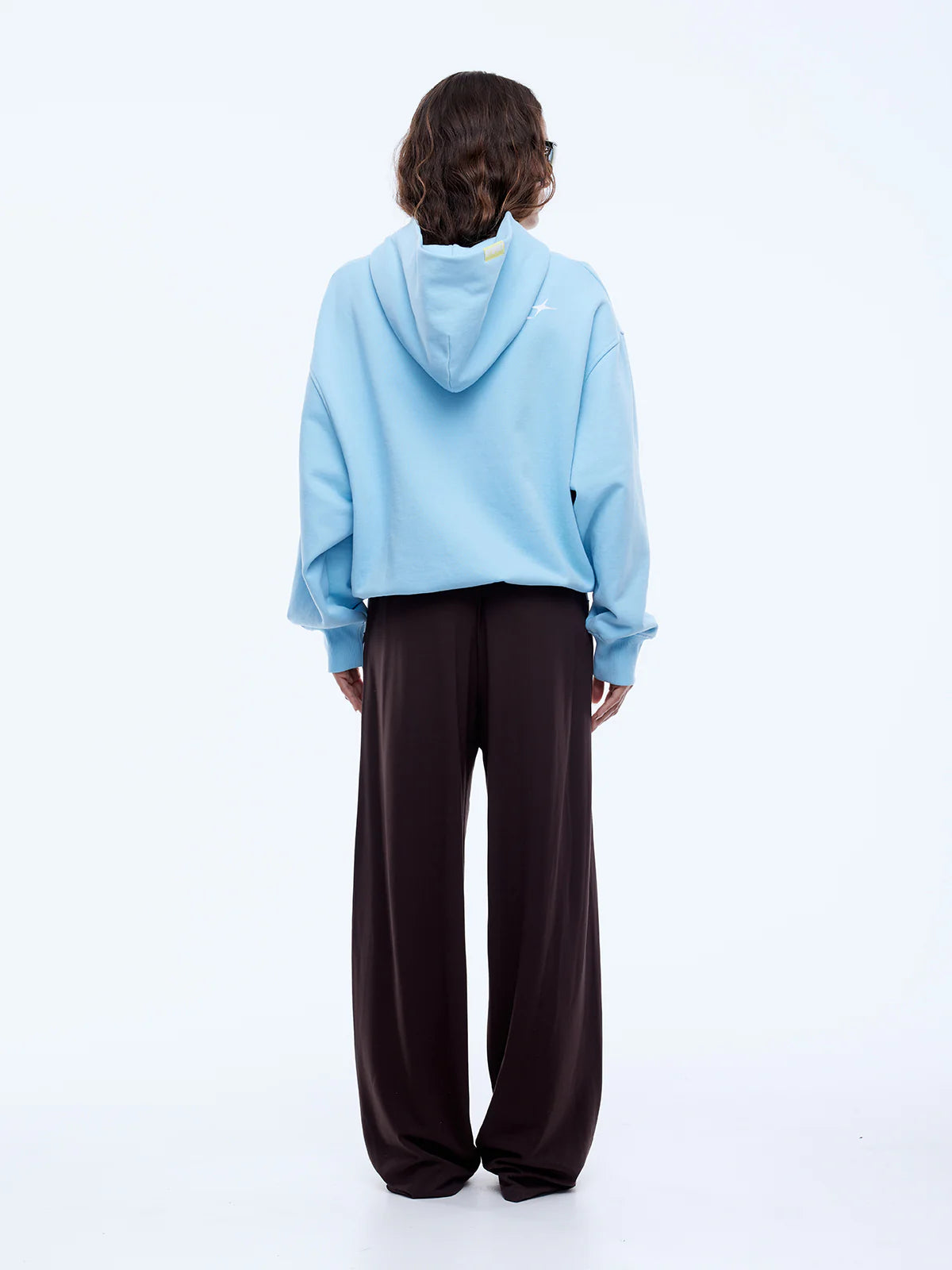 Person wearing a light blue hoodie and dark brown pants on a white background