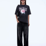 Person wearing a black t-shirt with a floral design and text, paired with black pants on a white background