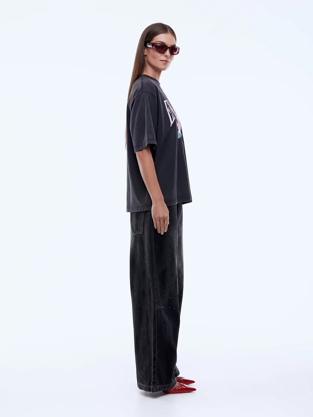 Person wearing a black oversized t-shirt and pants with red shoes on a white background