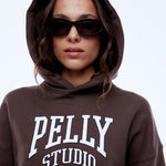 Person wearing a brown hoodie with 'PELLY STUDIO' text on a plain background