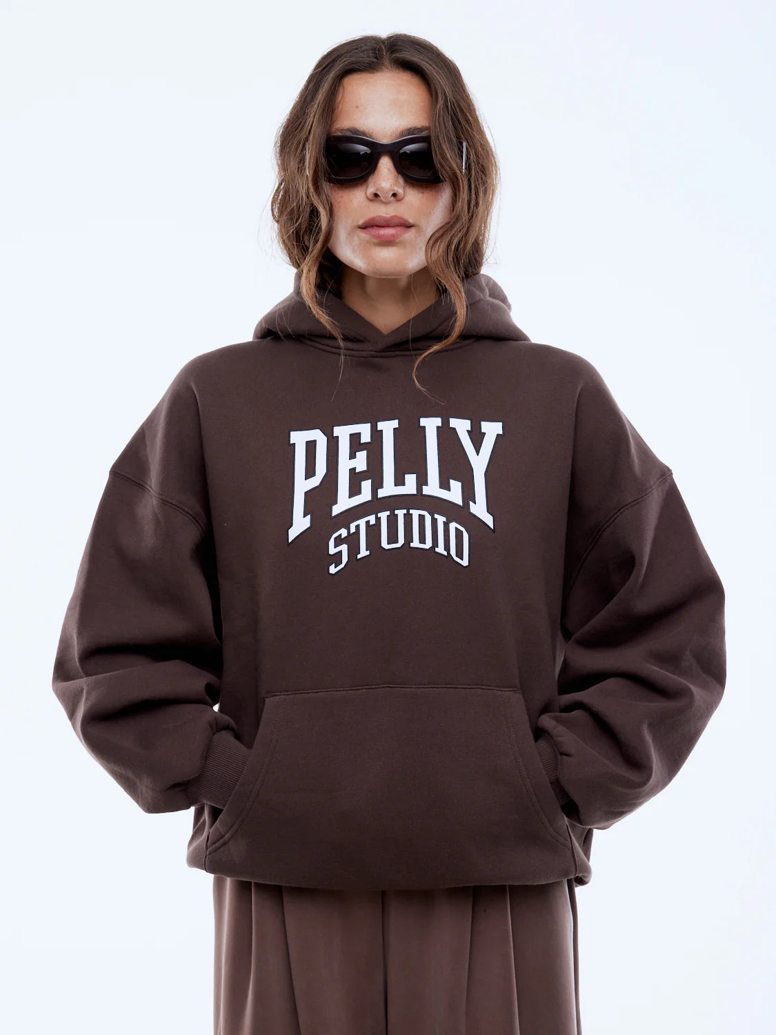 Person wearing a brown hoodie with 'PELLY STUDIO' text on a white background