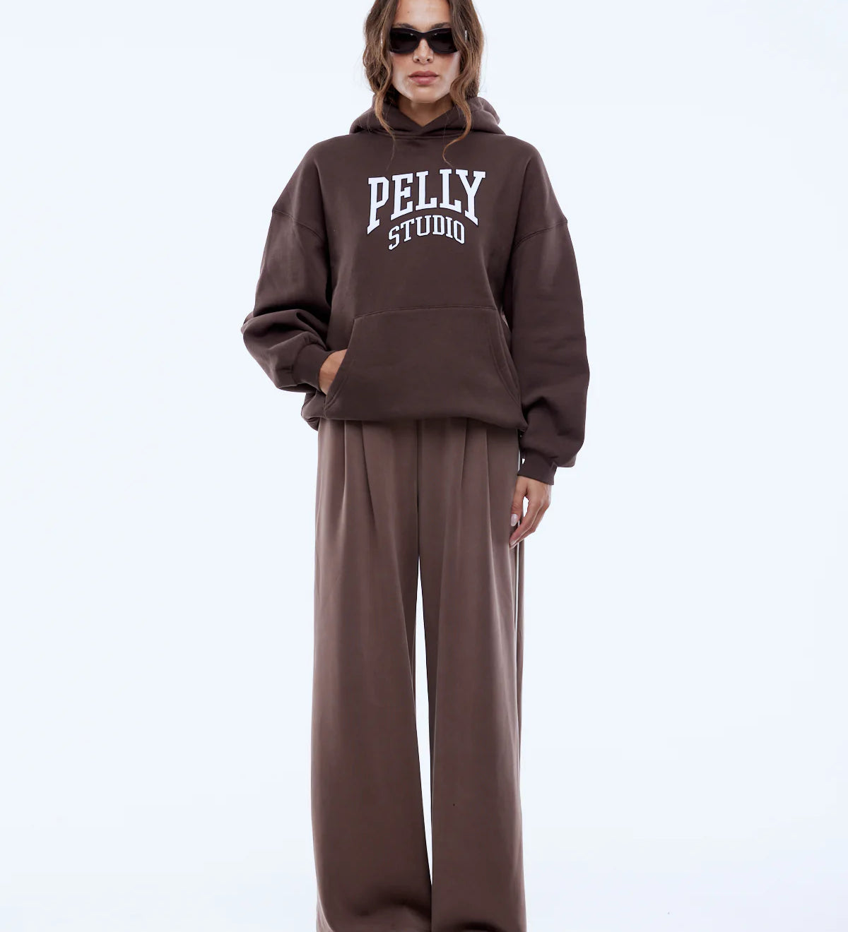 Person wearing a brown 'Pelly Studio' hoodie and pants on a white background