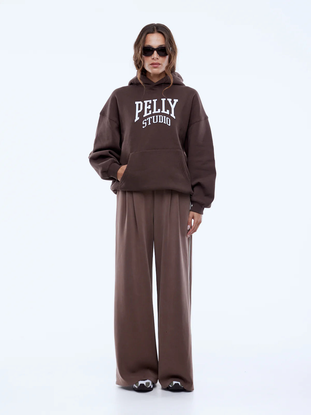 Person wearing a brown 'Pelly Studio' hoodie and pants on a white background