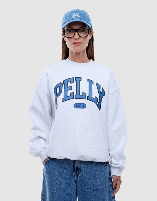 Person wearing a white sweatshirt with 'PELLY' branding, blue jeans, and a blue cap on a light gray background
