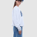 Person wearing a light gray sweatshirt with a graphic design and blue jeans on a white background