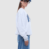 Person wearing a light gray sweatshirt with a graphic design and blue jeans on a white background