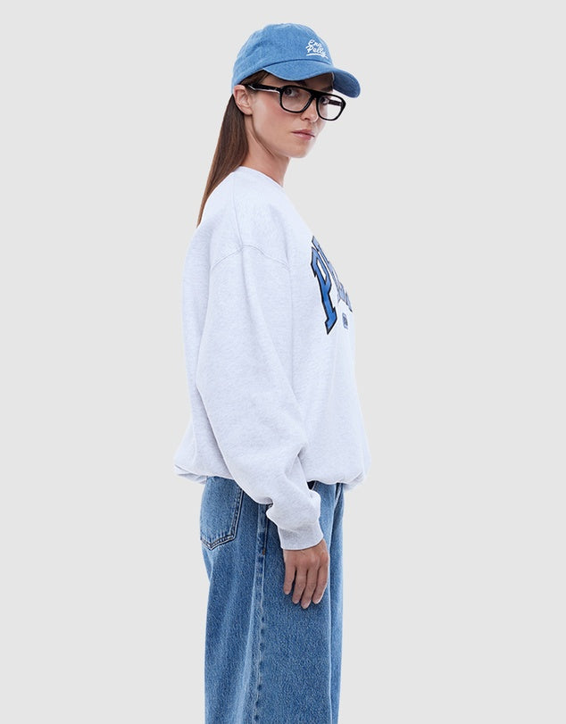 Person wearing a light gray sweatshirt with a graphic design and blue jeans on a white background