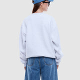 Person wearing a light gray sweatshirt and blue jeans with a blue cap on a plain background