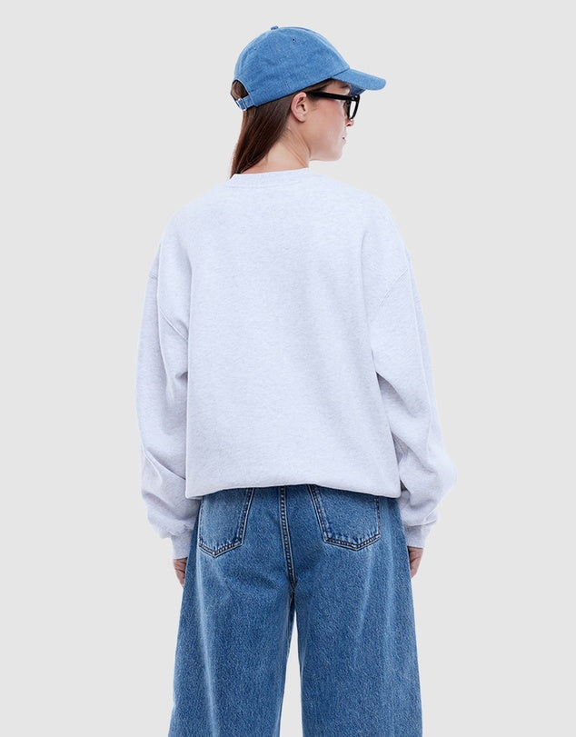 Person wearing a light gray sweatshirt and blue jeans with a blue cap on a plain background