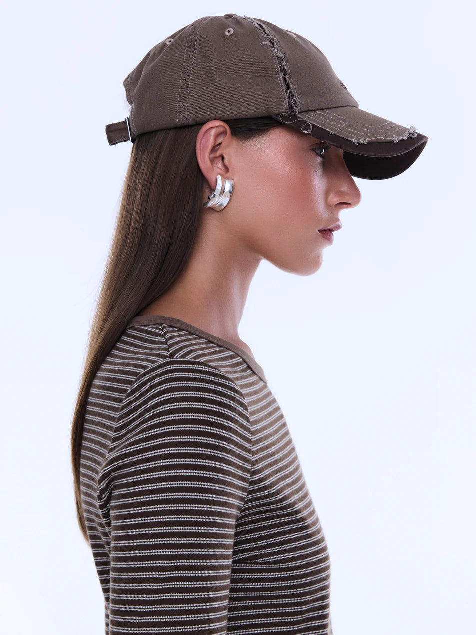 Woman wearing a brown baseball cap and striped shirt on a light gray background