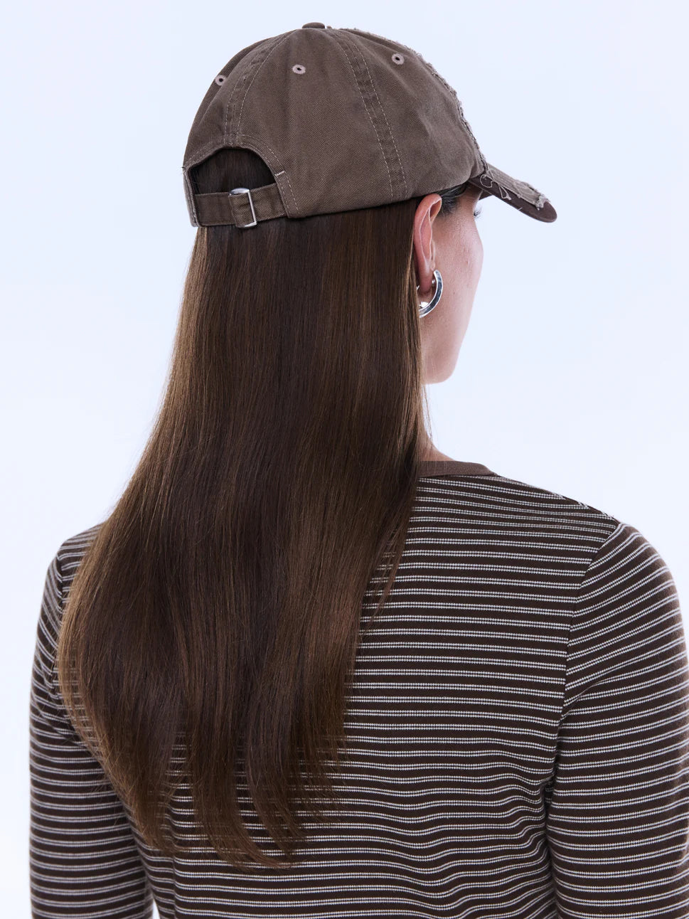 Person wearing a brown cap and striped shirt with long hair, on a white background