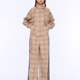 A model wearing a beige and brown plaid matching jacket and wide-leg pants set with black side stripes, styled with white-framed sunglasses against a plain white background.