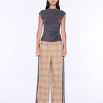 A model stands against a plain white studio background wearing a dark gray sleeveless top and beige plaid wide-leg pants with black side stripes.