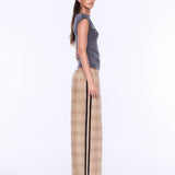 A woman stands in profile wearing a gray sleeveless top and beige plaid wide-leg pants with a black side stripe, photographed against a plain white studio background.