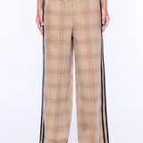 A person wearing wide-leg plaid pants in beige and brown with black side stripes, paired with a dark gray top and tan sandals, shown against a plain white studio background.