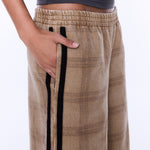 A close-up of a person wearing beige plaid wide-leg pants with black side stripes and a dark gray cropped top, shown against a plain white background.