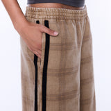 A close-up of a person wearing beige plaid wide-leg pants with black side stripes and a dark gray cropped top, shown against a plain white background.