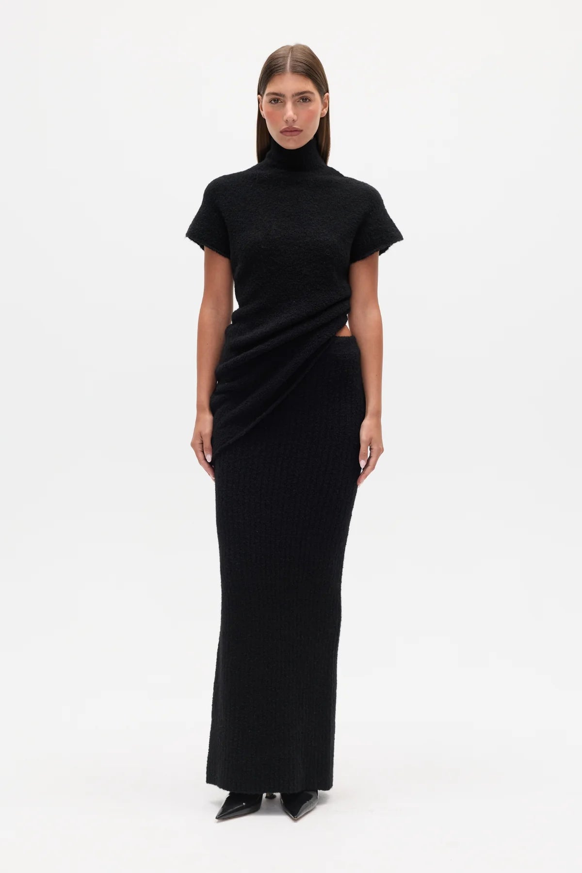 Woman wearing a black Top with a high neckline  and a long black skirt on a white background