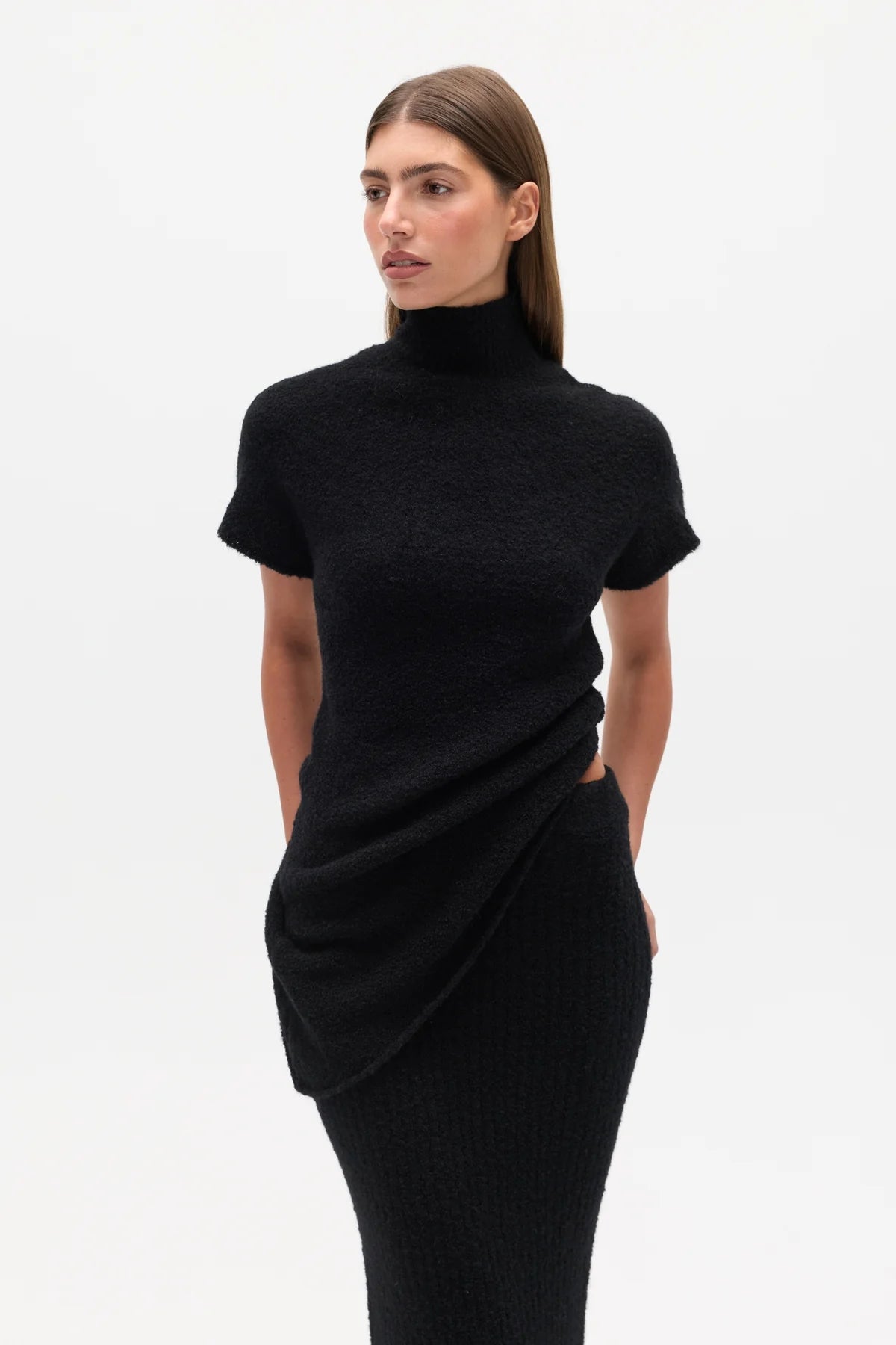 Woman wearing a black Top with a high neckline  and a long black skirt on a white background