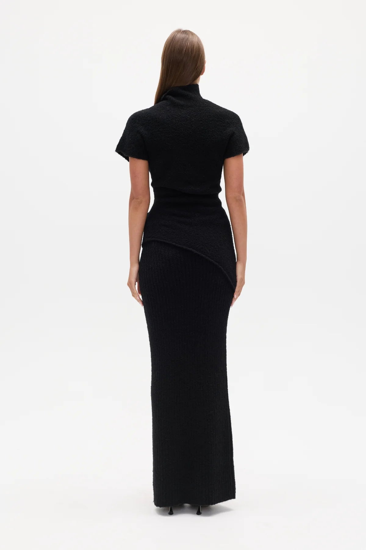 Woman wearing a black Top with a high neckline  and a long black skirt on a white background