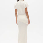Woman wearing a white high neck top and long white skirt on a white background