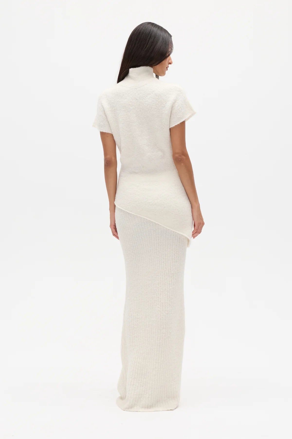 Woman wearing a white high neck top and long white skirt on a white background