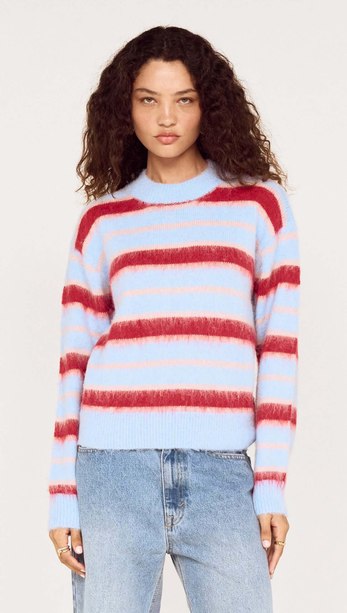 Woman wearing a multicolored striped sweater and jeans on a white background