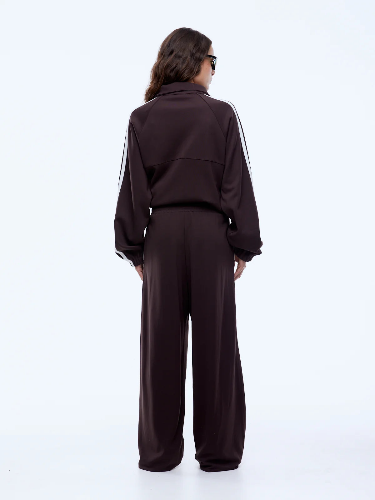 Person wearing a dark brown tracksuit with white stripes on a white background