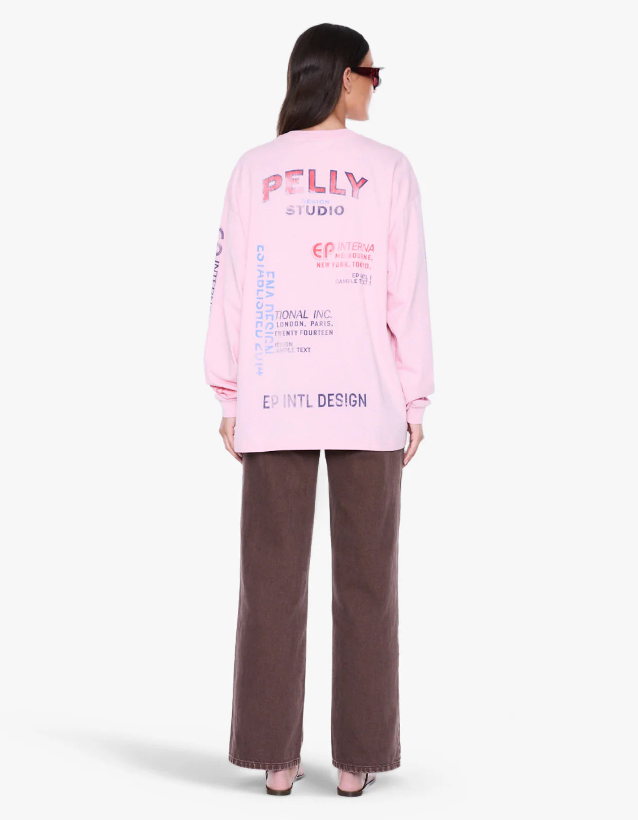 A model shown from the back wearing a light pink sweatshirt with colorful graphic text and dark brown wide-leg pants, photographed against a clean white background.