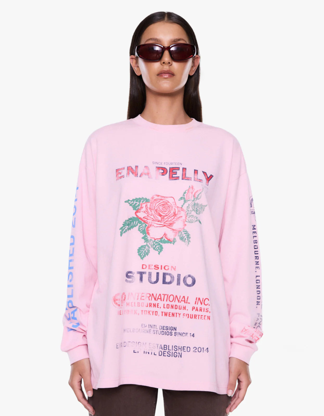 A model wearing a light pink long-sleeve graphic sweatshirt with a rose print and text, styled with dark sunglasses against a plain white background.