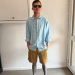 Person wearing a light blue shirt and beige shorts standing in a room with a white cabinet.