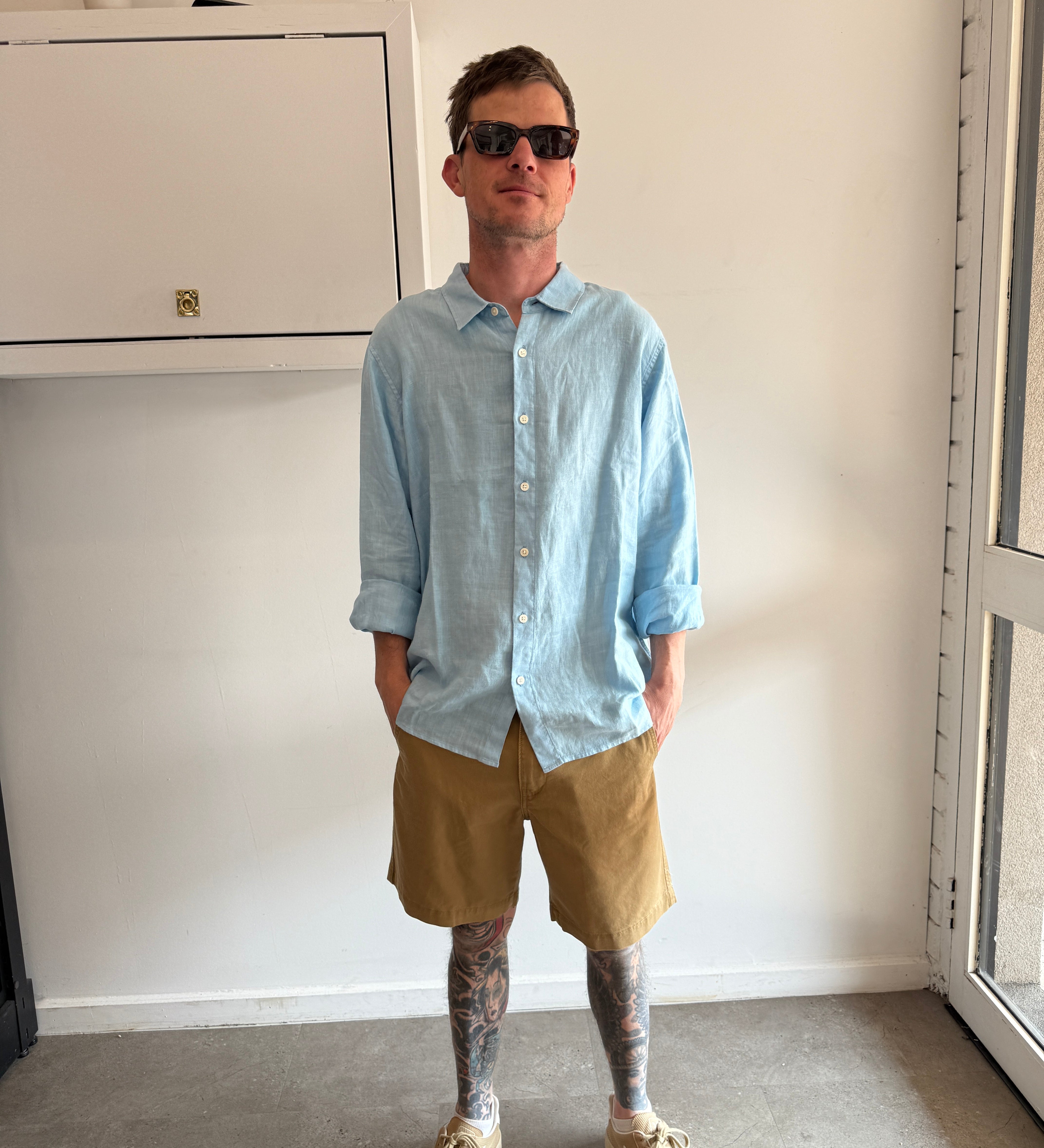 Person wearing a light blue shirt and beige shorts standing in a room with a white cabinet.