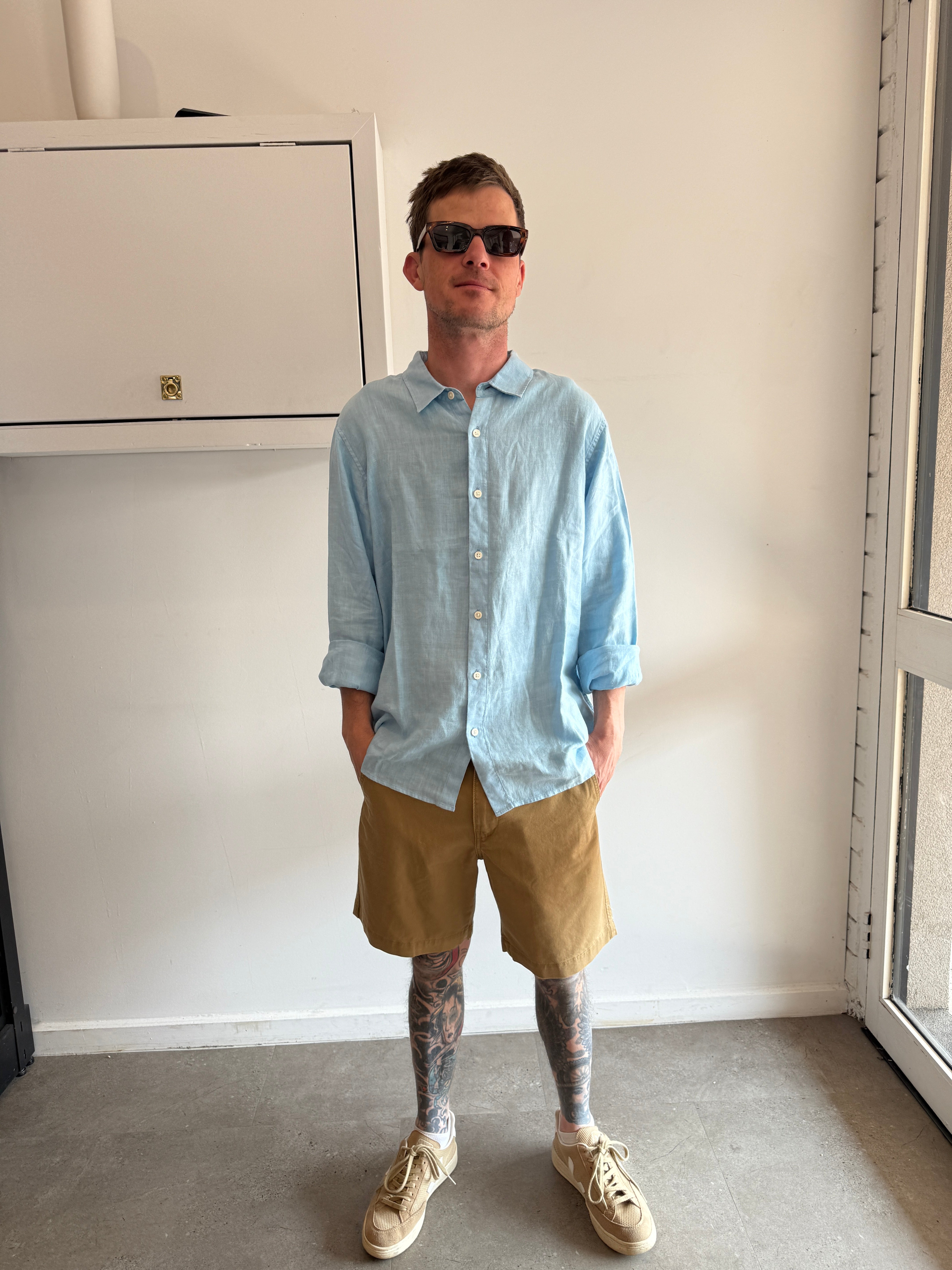 Person wearing a light blue shirt and beige shorts standing in a room with a white cabinet.
